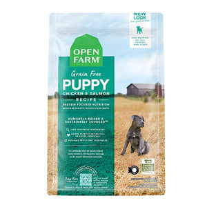 A bag of Open Farm Grain Free Puppy Recipe dog food. Humanely raised and sustainably sourced. A photo of a gray Pit Bull puppy standing in a field on a farm covers the bag, with a green bar behind the white text to highlight it.