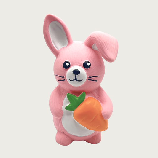 Small pink latex bunny dog toy with a folded ear, holding a carrot.