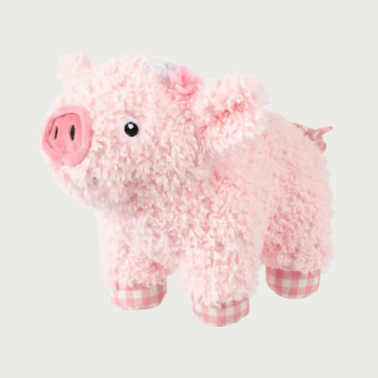 Pale pink, fluffy plush pig dog toy with a dark pink snout, small black & white embroidered eyes, tiny pink & pale blue flowers behind one ear, and pink-and-white gingham-patterned feet & tail.
