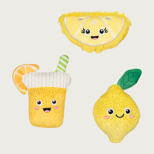 Three plush dog toys with a lemon theme, all with embroidered cute smiley faces. There is a yellow lemon wedge slice, a yellow whole lemon with a green leaf, and a yellow glass of lemonade with a green & white striped straw and lemon slice accent.