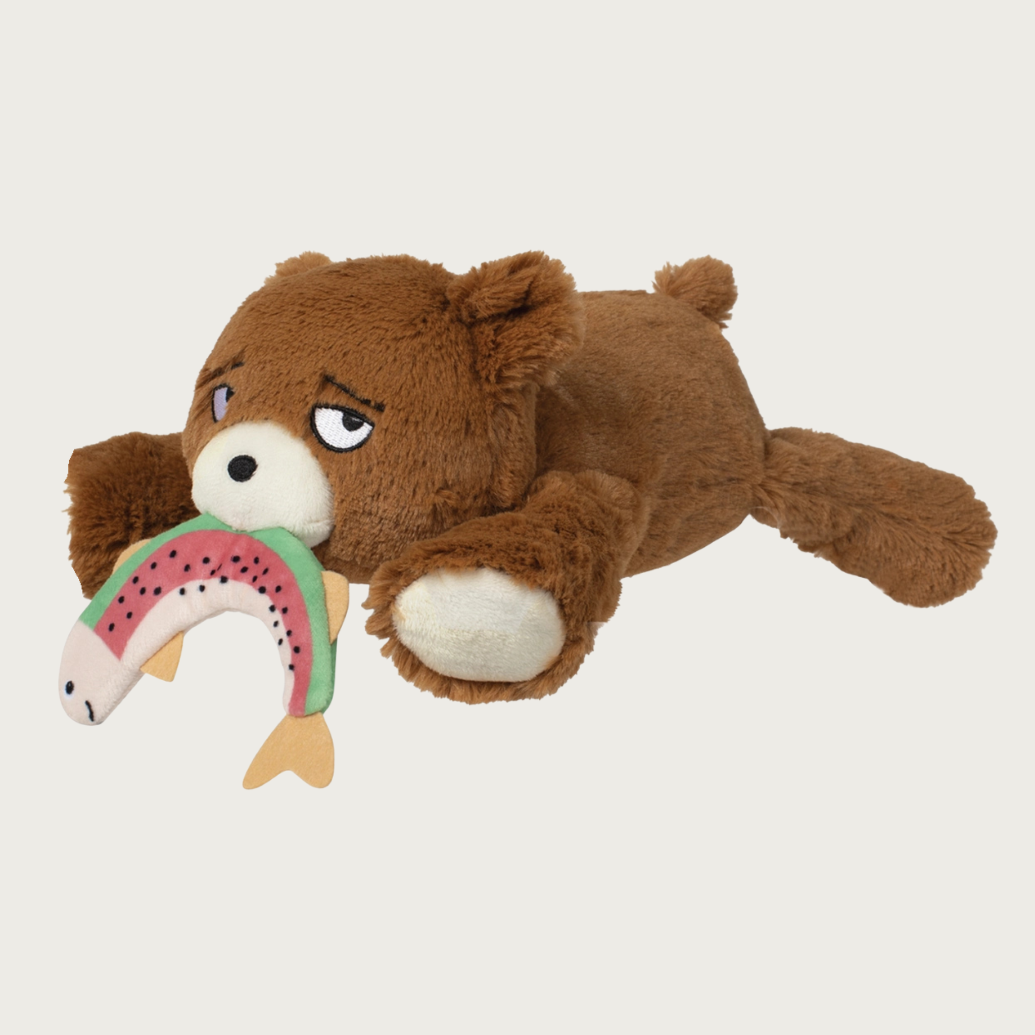 Plush brown bear dog toy laying on its tummy and holding a plush salmon in its mouth. Cute embroidered facial expression.