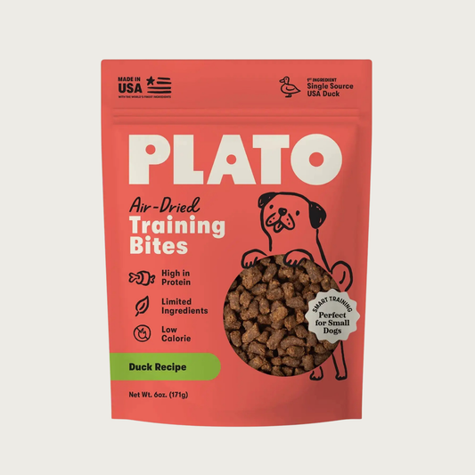 A 6 oz pouch of Plato Air-Dried Training Bites Duck Recipe dog treats. The packaging is a vibrant coral-red color with bold white text, a simple black line illustration of a dog, and a clear window showing the small, rectangular shaped brown treats inside. Made in USA, Single Source USA Duck, Perfect for Small Dogs.