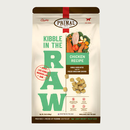 A 9 pound bag of chicken recipe Kibble in the Raw dog food from Primal Pet Foods. Text on bag reads "Kibble sized bites made with freeze-dried raw chicken" and "Serve like kibble. Nourish like raw." There is an image of fresh produce with a raw chicken breast, and a smaller image of the bite-sized morsels that are in the bag.