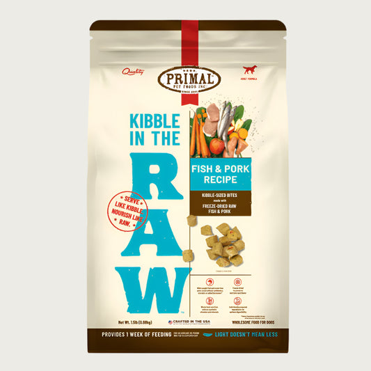 A 1.5 pound bag of fish & pork recipe Kibble in the Raw dog food from Primal Pet Foods. Text on bag reads "Kibble sized bites made with freeze-dried raw fish & pork" and "Serve like kibble. Nourish like raw." There is an image of fresh produce with raw pork chops and whole fish, and a smaller image of the bite-sized morsels that are in the bag.