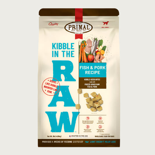 A 9 pound bag of fish & pork recipe Kibble in the Raw dog food from Primal Pet Foods. Text on bag reads "Kibble sized bites made with freeze-dried raw fish & pork" and "Serve like kibble. Nourish like raw." There is an image of fresh produce with raw pork chops and whole fish, and a smaller image of the bite-sized morsels that are in the bag.