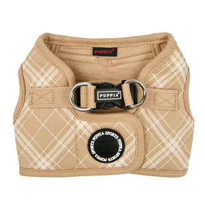 View of Puppia Corwin Step-In vest-style harness for dogs, laid flat. Interior and trim is tan colored, with the exterior cream plaid/check print on tan. Fastener clip on back is black. Accented with black rubber circle behind it, that says Puppia Sports in a repeating circular pattern.