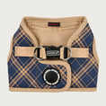 Load image into Gallery viewer, View of Puppia Corwin Step-In vest-style harness for dogs, laid flat. Interior and trim is tan colored, with the exterior tan plaid/check print on navy blue. Fastener clip on back is black. Accented with black rubber circle behind it, that says Puppia Sports in a repeating circular pattern.
