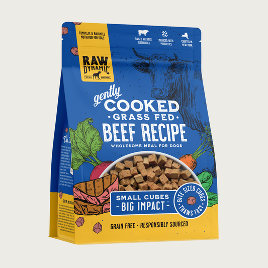 Raw Dynamic Gently Cooked Grass Fed Beef Recipe wholesome meal for dogs, packaged in a deep blue bag with illustrations of a cow and vegetables. Additional text reads: small cubes, big impact. Bite sized cubes thaws fast. Complete & balanced nutrition for dogs. Grain free, responsibly sourced. Half-moon shaped transparent window on bottom 1/3 of bag shows small, tan cubes of food.