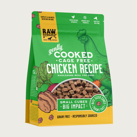 Raw Dynamic Gently Cooked Cage Free Chicken Recipe wholesome meal for dogs, packaged in a bright green bag with illustrations of a chicken and vegetables. Additional text reads: small cubes, big impact. Bite sized cubes thaws fast. Complete & balanced nutrition for dogs. Grain free, responsibly sourced. Half-moon shaped transparent window on bottom 1/3 of bag shows small, tan cubes of food.