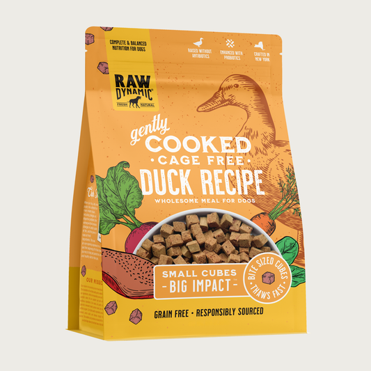 Raw Dynamic Gently Cooked Cage Free Duck Recipe wholesome meal for dogs, packaged in a light orange bag with illustrations of a duck and vegetables. Additional text reads: small cubes, big impact. Bite sized cubes thaws fast. Complete & balanced nutrition for dogs. Grain free, responsibly sourced. Half-moon shaped transparent window on bottom 1/3 of bag shows small, tan cubes of food.