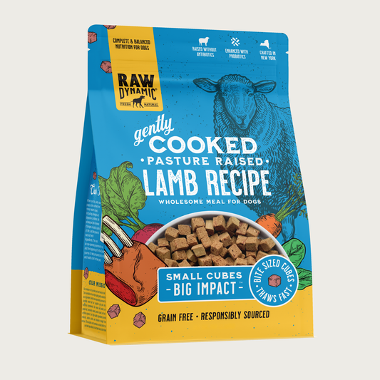 Raw Dynamic Gently Cooked Pasture Raised Lamb Recipe wholesome meal for dogs, packaged in a medium blue bag with illustrations of a sheep and vegetables. Additional text reads: small cubes, big impact. Bite sized cubes thaws fast. Complete & balanced nutrition for dogs. Grain free, responsibly sourced. Half-moon shaped transparent window on bottom 1/3 of bag shows small, tan cubes of food.