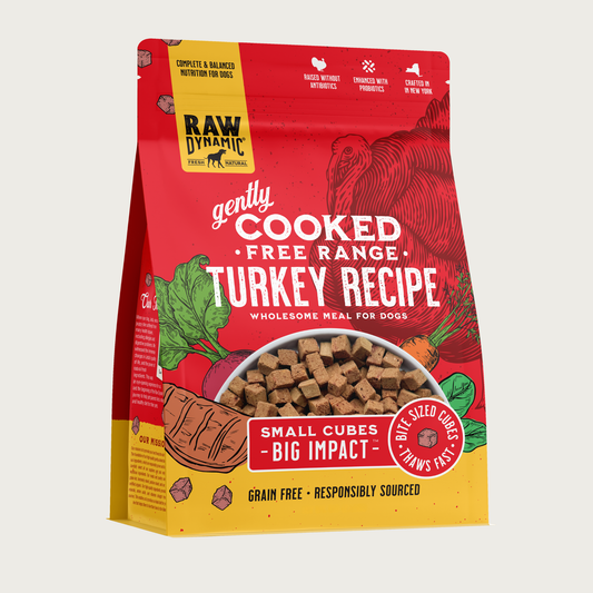 Raw Dynamic Gently Cooked Free Range Turkey Recipe wholesome meal for dogs, packaged in a red bag with illustrations of a turkey and vegetables. Additional text reads: small cubes, big impact. Bite sized cubes thaws fast. Complete & balanced nutrition for dogs. Grain free, responsibly sourced. Half-moon shaped transparent window on bottom 1/3 of bag shows small, tan cubes of food.