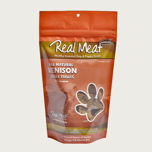 12 oz tan/orange bag of all natural venison jerky dog & puppy treats from The Real Meat Company. 95% venison, no fillers. Small, clear, paw print shaped window on bag shows product inside - brown, rectangular shaped treats.