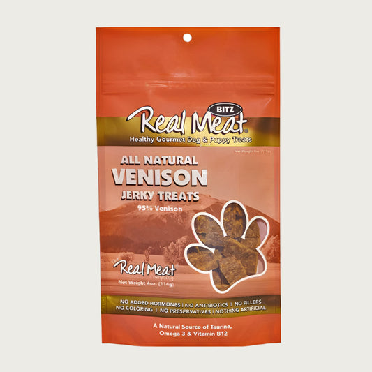 4 oz tan/orange bag of all natural venison jerky dog & puppy treats from The Real Meat Company. 95% venison, no fillers. Small, clear, paw print shaped window on bag shows product inside - brown, rectangular shaped treats.
