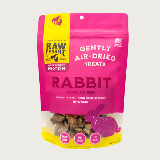 Pink package of Raw Dynamic Gently Air-Dried Rabbit Treats for dogs. Small transparent window on the bottom of the bag shows small, brown treats.