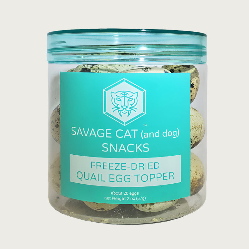 A 2 oz clear plastic container, filled with freeze-dried quail eggs by Savage Cat. Snacks for cats and dogs, about 20 eggs per container. Eggs are very small, and have a tan color with brown speckles.