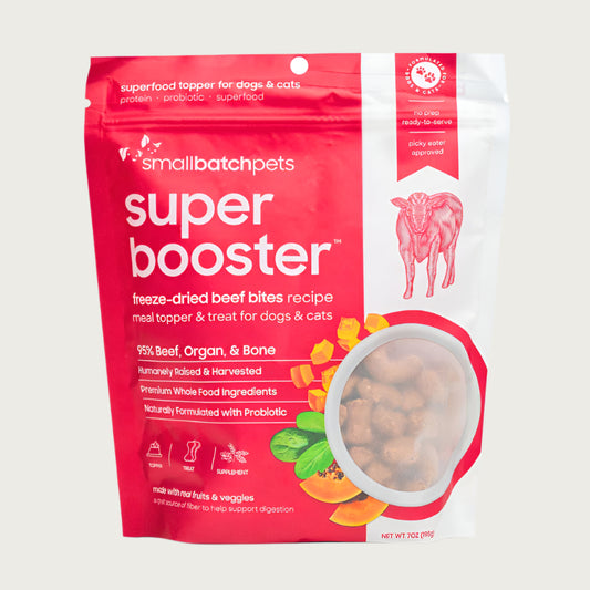 A red and white, 7 ounce bag of Smallbatch Super Booster freeze-dried raw beef bites recipe for dogs and cats. Can be used as a meal topper or treat. The bag has a small, clear window showing bite-sized treat pieces, about 1/2" to 1" long.