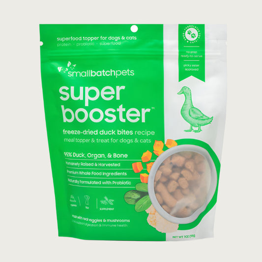 A green and white, 7 ounce bag of Smallbatch Super Booster freeze-dried raw duck bites recipe for dogs and cats. Can be used as a meal topper or treat. The bag has a small, clear window showing bite-sized treat pieces, about 1/2" to 1" long.