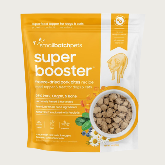 A yellow and white, 7 ounce bag of Smallbatch Super Booster freeze-dried raw pork bites recipe for dogs and cats. Can be used as a meal topper or treat. The bag has a small, clear window showing bite-sized treat pieces, about 1/2" to 1" long.