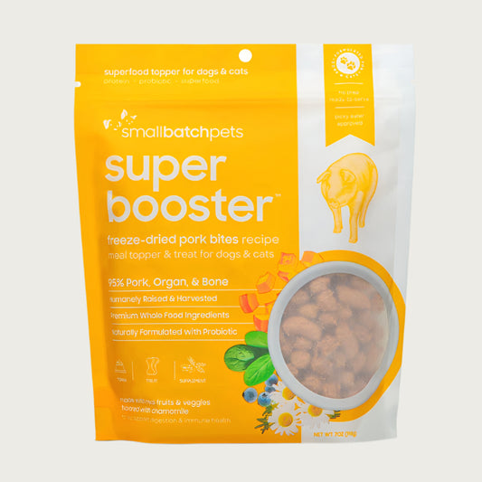 A yellow and white, 7 ounce bag of Smallbatch Super Booster freeze-dried raw pork bites recipe for dogs and cats. Can be used as a meal topper or treat. The bag has a small, clear window showing bite-sized treat pieces, about 1/2" to 1" long.