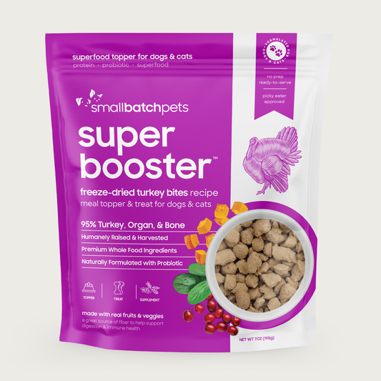 A purple and white, 7 ounce bag of Smallbatch Super Booster freeze-dried raw turkey bites recipe for dogs and cats. Can be used as a meal topper or treat. The bag has a small, clear window showing bite-sized treat pieces, about 1/2" to 1" long.