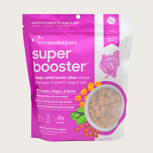 A hot pink and white, 7 ounce bag of Smallbatch Super Booster freeze-dried raw turkey bites recipe for dogs and cats. Can be used as a meal topper or treat. The bag has a small, clear window showing bite-sized treat pieces, about 1/2" to 1" long.