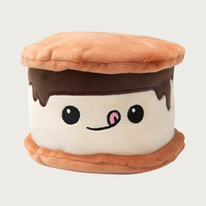 Plush s'more dog toy, with brown "graham crackers" on the top and bottom, with cream "marshmallow" and dripping "chocolate" down its face. Cute embroidered expression with big eyes and pink tongue licking its lips.