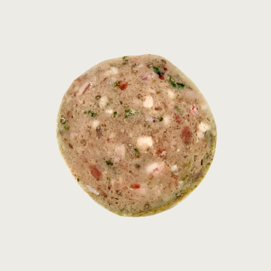 A close-up view of a Solutions Pet Products slider, that is light reddish brown in color. Pieces of green vegetables, small chunks of meat and either bone or fat are visible.