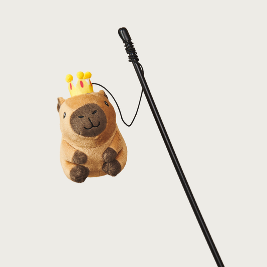 Plush, plump, brown capybara cat toy wearing a crown, at the end of a string attached to a black plastic wand. Has a cute embroidered facial expression.