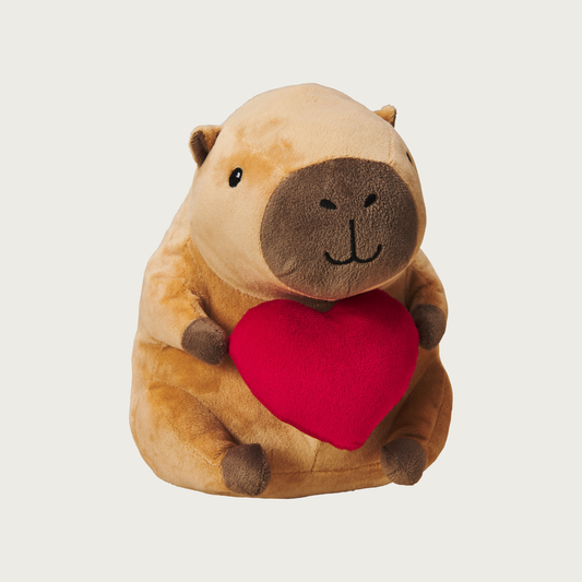 Plush, plump, brown capybara dog toy holding a red plush heart in its hands. Has a cute embroidered facial expression.