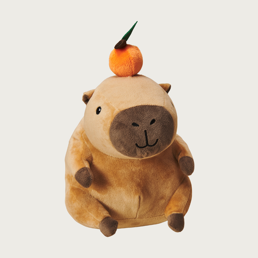 Plush, plump, brown capybara dog toy with a small plush orange "balanced" on his head. Has a cute embroidered facial expression.