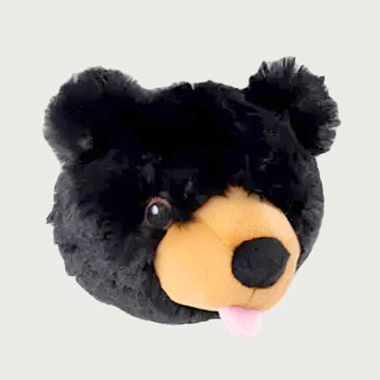 A plush ball in the shape of a black bear's head. It has embroidered eyes, tan muzzle, black nose and a pink tongue that is playfully sticking out of its mouth.