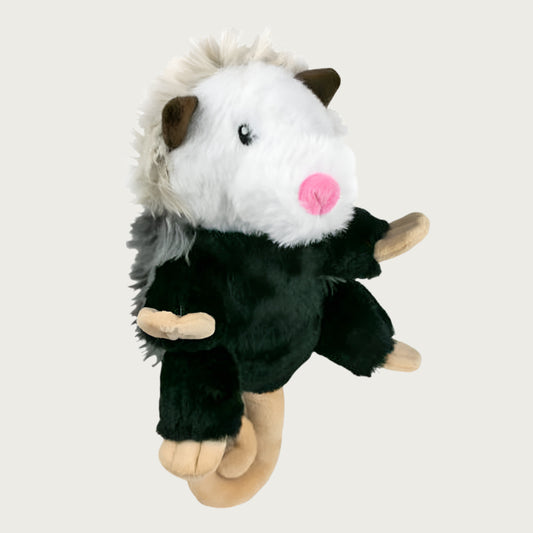 Side view of shaggy plush possum dog toy from Tall Tails. This realistic looking toy has a black plush body with white head, embroidered eyes, pink nose, brown ears and curly beige tail. Its back has two tones of shaggy gray faux fur.