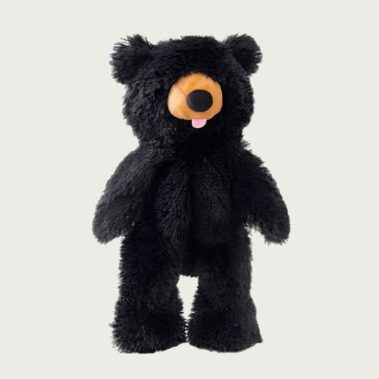 A full body black bear dog toy. It is covered in shaggy black plush, with a tan muzzle, black nose, and pink tongue playfully sticking out of the bear's mouth.