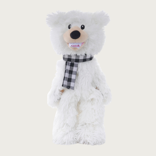 A full body polar bear dog toy. It is covered in shaggy white plush, with a tan muzzle, black nose & eyes, and a toothy grin. It's wearing a black & white buffalo check scarf.