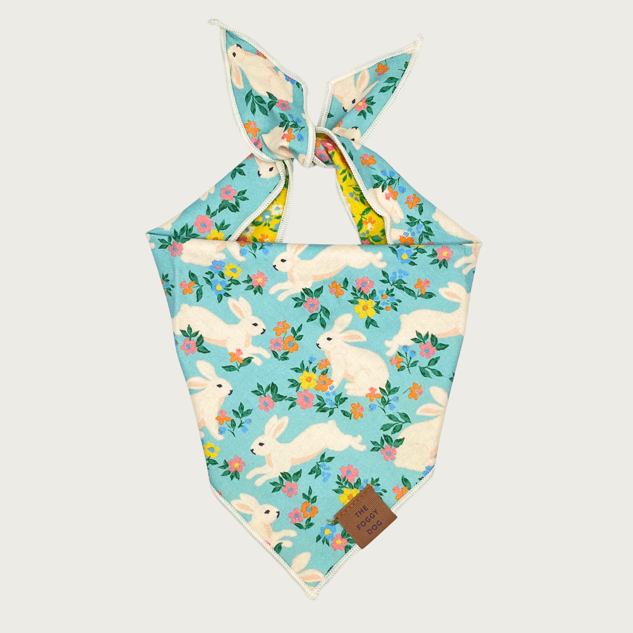 Easter-themed dog bandana. Base color is light aqua blue, pattern features ivory bunnies hopping amongst multicolored pansies.