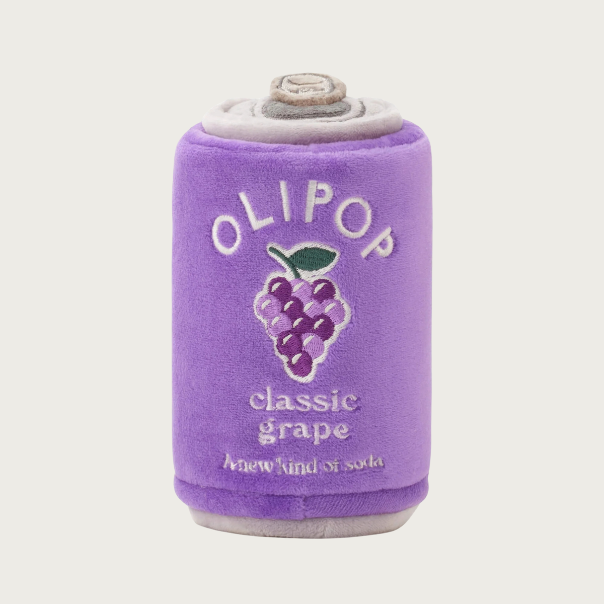 A plush soda can-shaped dog toy in purple, featuring embroidered text that reads 'OLIPOP classic grape' and an embroidered grape bunch graphic.