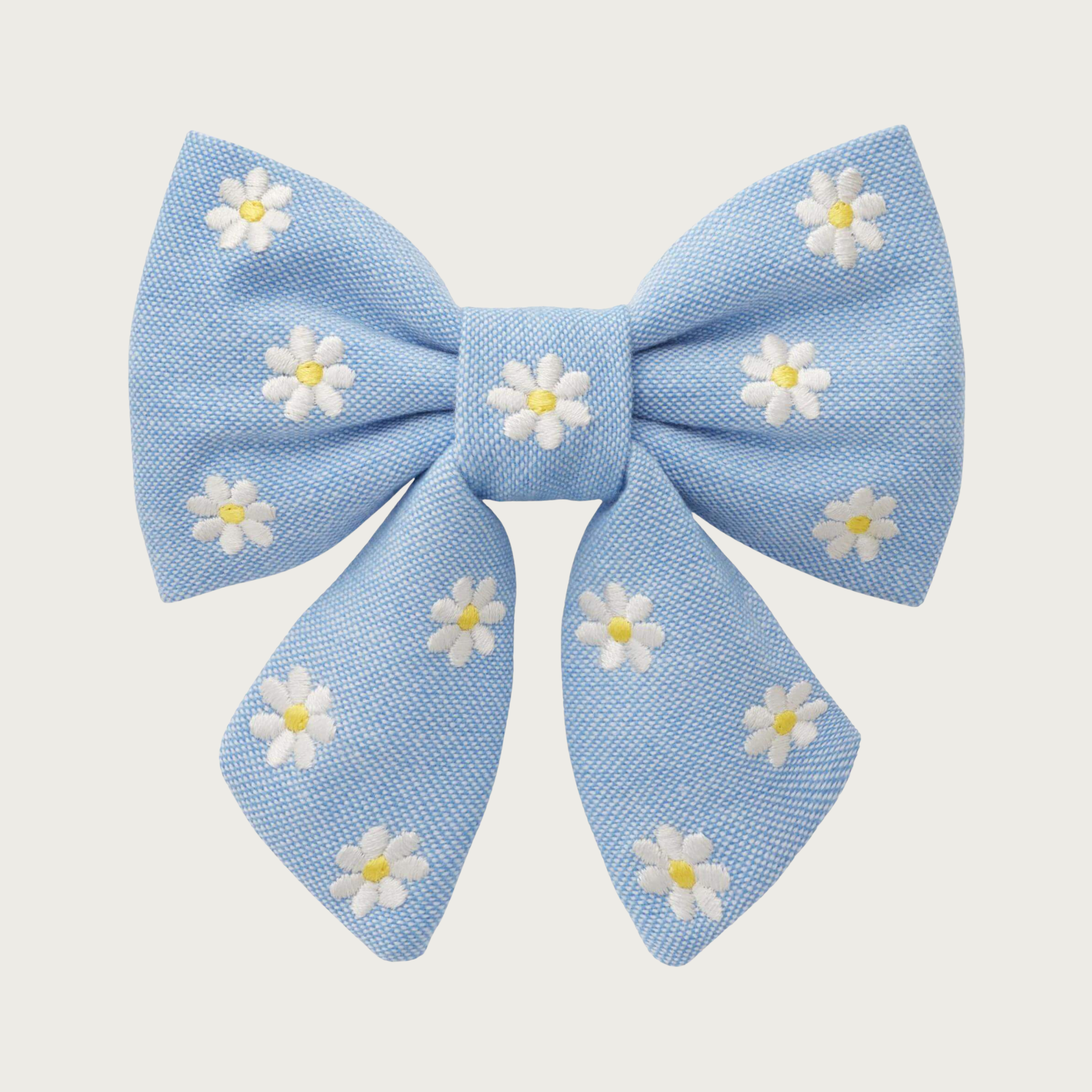 Light blue Oxford cloth lady bow tie for dogs, with embroidered white daisies with yellow centers, stitched evenly across the entire bow. Looks like a hair bow for a person, with the center bow tie and ends hanging down.