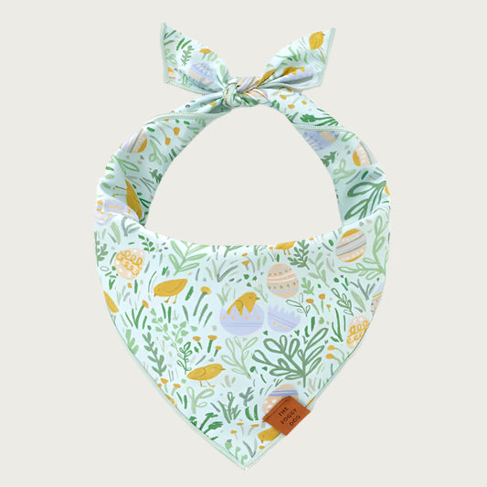 Easter-themed dog bandana. Background color is pastel mint green, print features pastel Easter eggs and yellow chicks, in a grassy field.