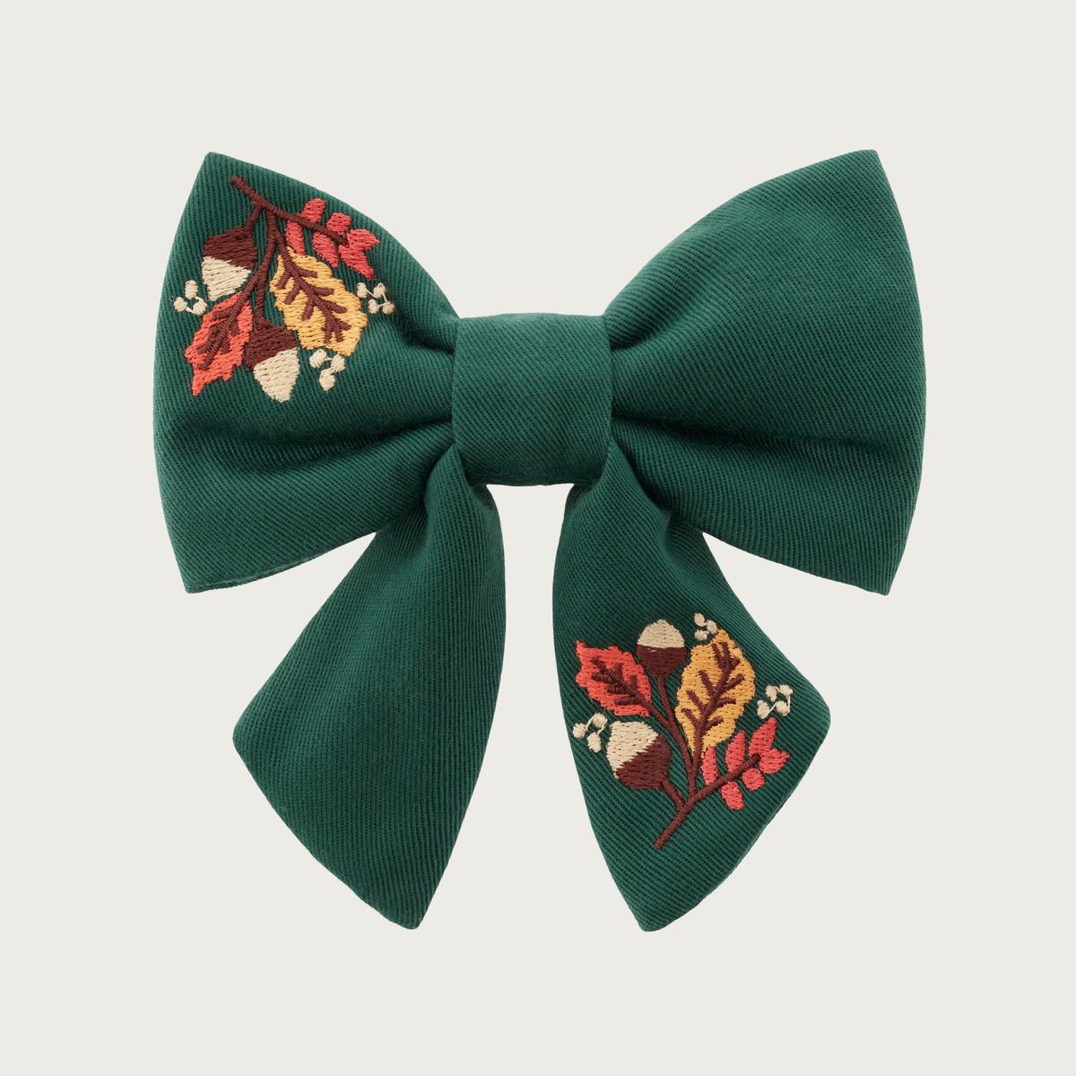 Forest green lady bow tie for dogs, with two embroidered sections featuring autumn leaves & acorns, in the top left and bottom right of the bow. Looks like a hair bow for a person, with the center bow tie and ends hanging down.
