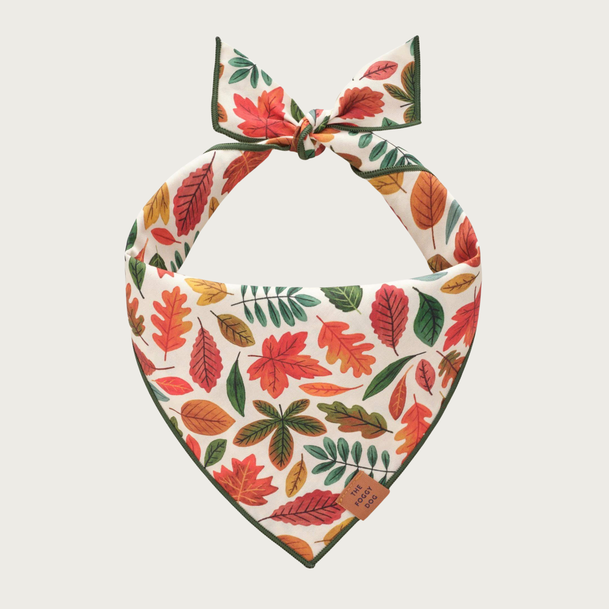 A dog bandana with an autumn leaf pattern, featuring a variety of red, orange, green, and yellow leaves on a cream background, tied at the top.