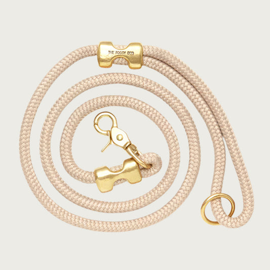 Coiled, light beige rope dog leash with brass hardware. Fastened on both ends with brass clamps, instead of stitching. O-ring is in the handle part of the leash, with lobster claw style of clasp to connect to collar or harness.