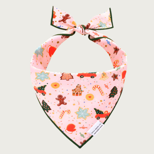 Christmas-themed dog bandana with traditional holiday icons on a pale pink background.