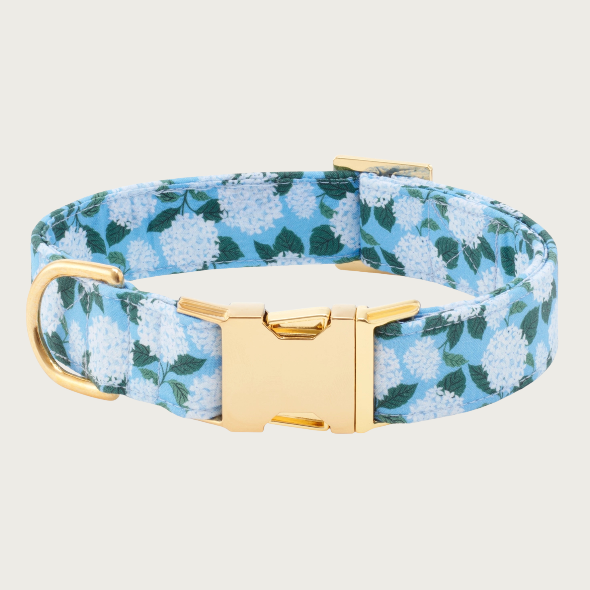Medium blue colored dog collar with a light bluish-white hydrangea print accented with dark green leaves. Collar features gold-toned metal hardware.