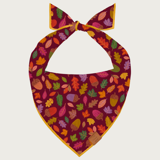 Dog bandana with multicolored autumn leaf & acorn pattern on a cranberry colored background.