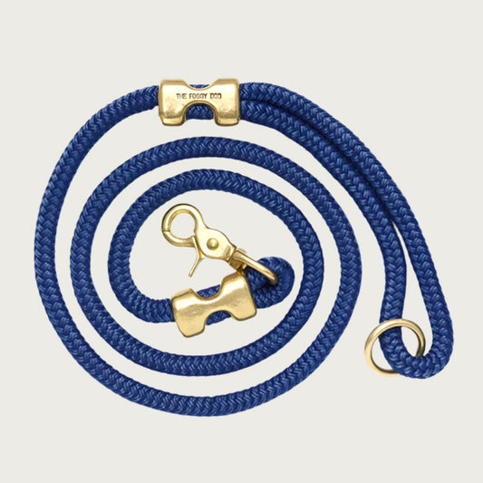 Coiled, navy blue rope dog leash with brass hardware. Fastened on both ends with brass clamps, instead of stitching. O-ring is in the handle part of the leash, with lobster claw style of clasp to connect to collar or harness.