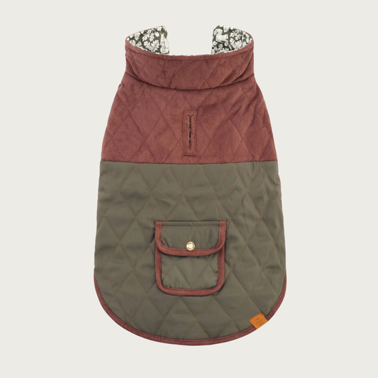 A quilted dog coat with a color-blocked design, featuring a dark brown upper section and a muted olive green lower section. It has a small pocket with a snap button closure centered in the olive green section, and a patterned lining visible at the collar. There is a trimmed leash opening near the shoulder blades.