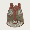 Load image into Gallery viewer, Underside of the Olive Reversible Dog Jacket, showing its snap closure along the chest, stand-up, foldable collar, and olive green & cream squirrel, leaf, and acorn print lining, with two generously sized arm holes.
