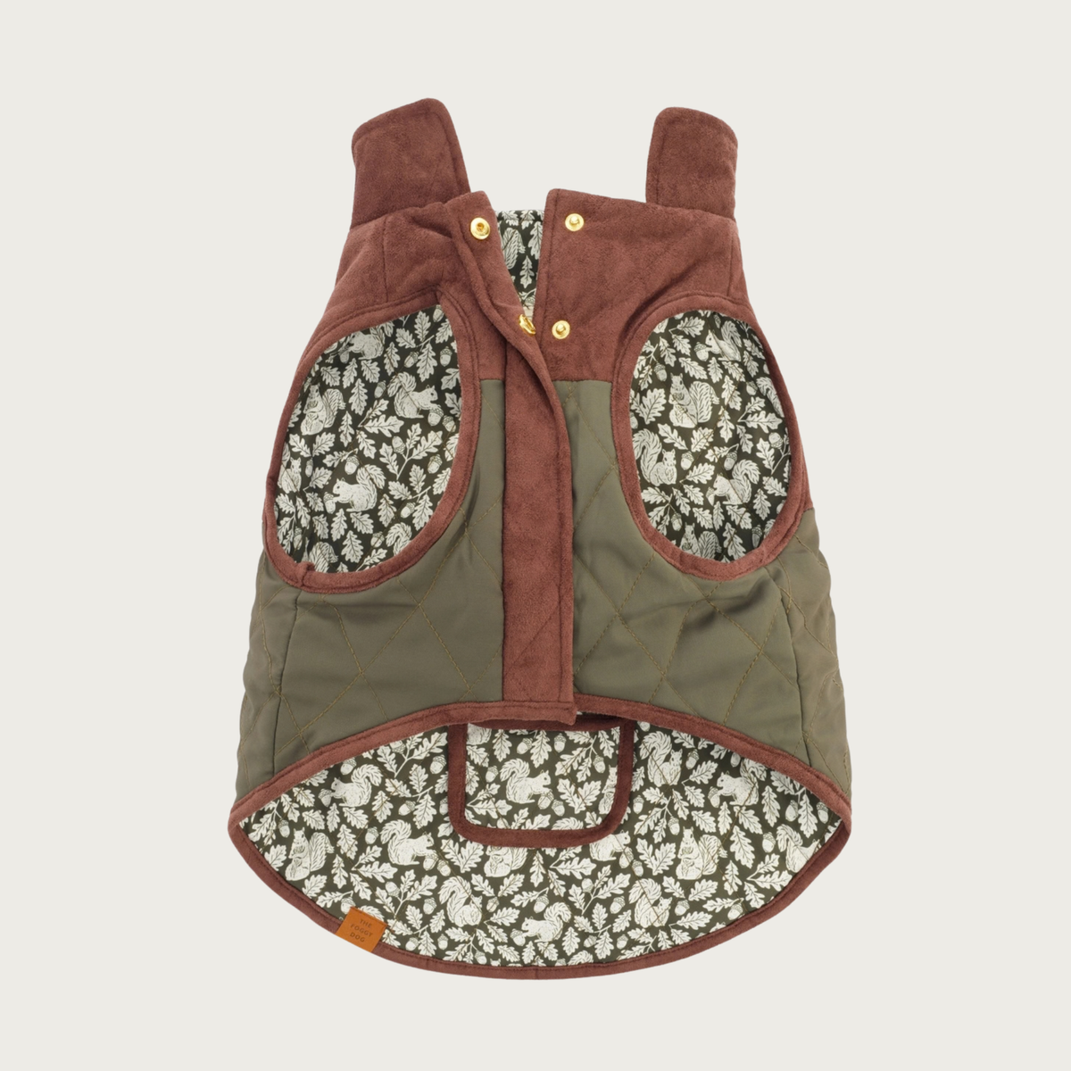 Underside of the Olive Reversible Dog Jacket, showing its snap closure along the chest, stand-up, foldable collar, and olive green & cream squirrel, leaf, and acorn print lining, with two generously sized arm holes.