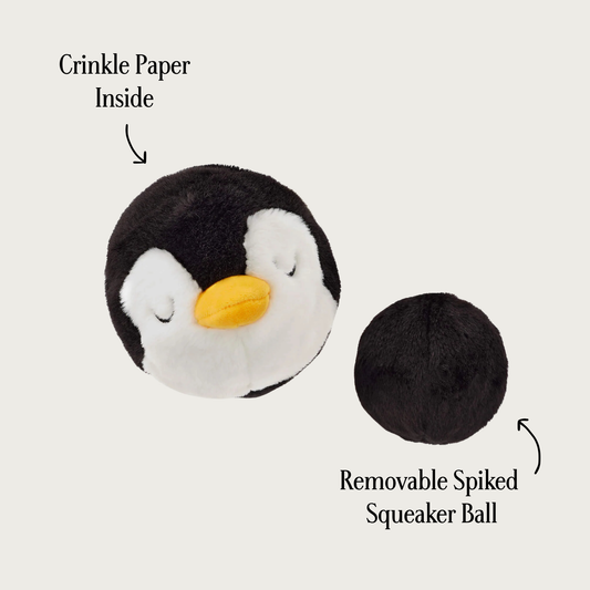 Plush penguin ball dog toy, with removable spiked squeaker ball next to it. Ball has black plush covering it. Text pointing to the penguin says "crinkle paper inside" and text pointing to the smaller ball says "removable spiked squeaker ball".